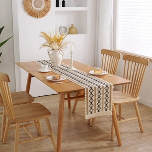 Chemin de table bohème avec motifs losanges et pompons sur une table en bois naturel