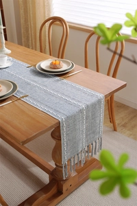 Close-up of blue-grey table runner featuring white wave embroidery and handcrafted tassels