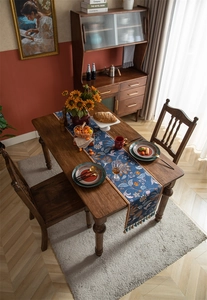 Détail d'un chemin de table rétro avec fleurs et franges sur une table en bois massif