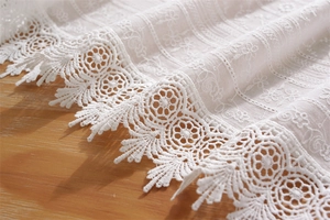 Detailed close-up of white floral lace embroidery on high-quality cotton tablecloth fabric