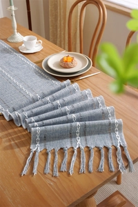 Detailed view of jacquard table runner with white embroidery and manual tassels