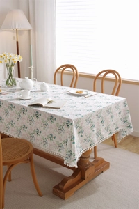 Close-up of cotton tablecloth featuring green leaf prints and white pom-pom fringe details