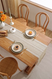 Detail of hollow jacquard table runner with handmade tassels on wooden dining table