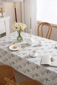 Detail of floral printed cotton tablecloth featuring green leaves and white pom-pom trim