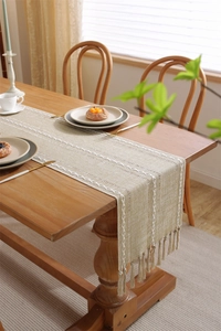 Close-up of beige jacquard table runner with white woven patterns and elegant fringe
