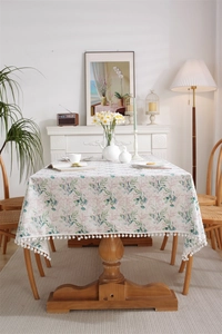 Detail of floral rectangular tablecloth featuring green leaves, red berries, and pom-pom edges