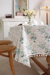 Detail of cotton tablecloth with green leaf print and white pom-pom fringe trim