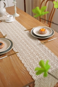 Detail of cream crochet lace table runner with hollow floral pattern and fringe