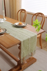 Close-up of green jacquard table runner with white woven lines and handmade tassels