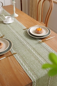 Detail of green jacquard table runner with white woven patterns on a wooden dining table