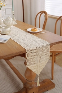 Detail of cream crochet table runner showing intricate floral lace patterns and tassels