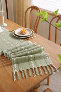 Detail of green woven table runner with white embroidery patterns and tassel edges