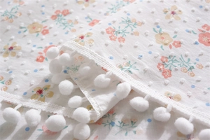 Detail of floral cotton tablecloth with Swiss dot texture and white pom-pom fringe trim