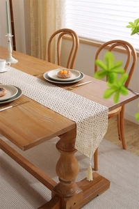 Close-up of beige crochet table runner with intricate lace patterns and tassel edges