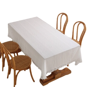White cotton lace tablecloth with hollow embroidery and elegant fringe tassels on a table