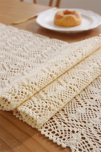 Macro detail of beige crochet table runner with lace patterns and scalloped edges
