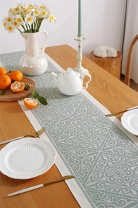 Detail of green damascus jacquard table runner with fringe on a wooden dining table