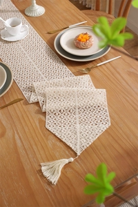 Detail of beige lace table runner featuring geometric hollow patterns and tassels