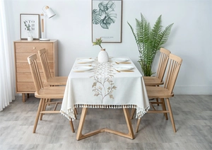 Close-up of elegant floral embroidery and tassel fringe on a cream linen tablecloth