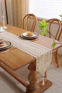 Close-up of cream crochet lace table runner with hollow floral pattern and elegant tassels