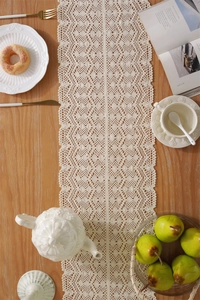 Close-up of beige crochet table runner with wave edges and hollow diamond lace patterns