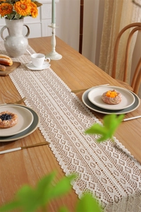 Detailed view of cream crochet lace table runner with hollow floral patterns and tassels