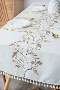 Detail of embroidered floral patterns and white tassels on a cream linen tablecloth