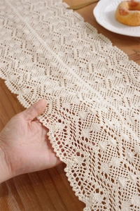 Close-up of beige crochet table runner with wave edges and intricate lace knitting