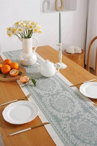 Detailed close-up of teal jacquard table runner with white floral pattern and neat edging