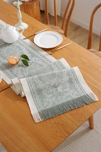 Detailed texture of sage green floral jacquard table runner with white tassel fringe