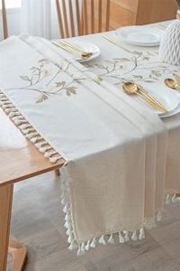Detail of embroidered plant pattern and handmade tassels on cotton linen table runner