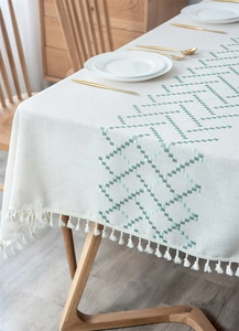 Detailed view of mint green geometric embroidery and beige tassels on linen tablecloth