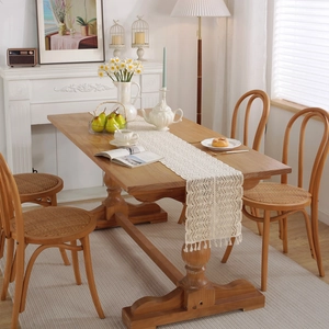 Beige crochet lace table runner with hollow wave pattern and tassels on wood table