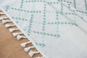 Detailed view of mint green geometric plaid embroidery and white fringe on a table runner