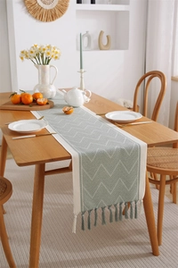 Close-up of sage green jacquard table runner with white chevron patterns and tassel fringe