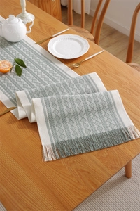 Detail of sage green geometric jacquard table runner with delicate fringe on wooden table