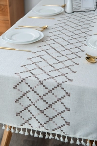 Detail of embroidered geometric patterns and fringe edges on a cream linen tablecloth