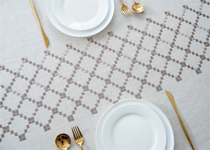 Macro view of geometric diamond embroidery on beige linen tablecloth with gold cutlery