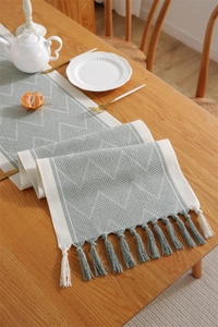 Detail of sage green woven table runner with geometric waves and fine tassel trim