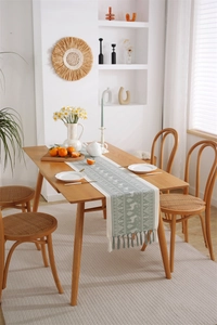 Detail of forest jacquard table runner with handmade tassels on wooden dining table