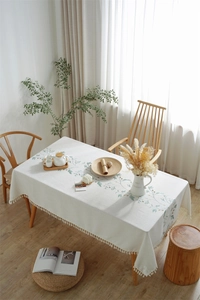 Detail of embroidered floral vine patterns and white cotton tassels on linen tablecloth
