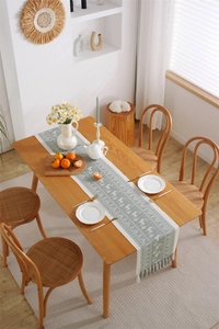 Detail of sage green jacquard table runner with white forest pattern and tassels