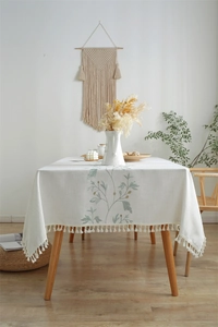 Detailed close-up of cream cotton linen tablecloth with leaf embroidery and white tassels