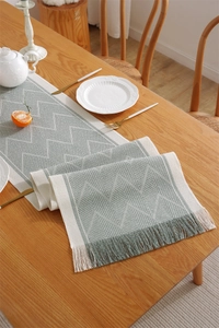 Detail of green geometric jacquard table runner with handmade tassels on wooden dining table