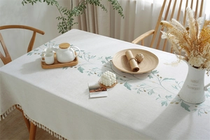 Detailed close-up of rectangular linen tablecloth with green floral print and white tassels