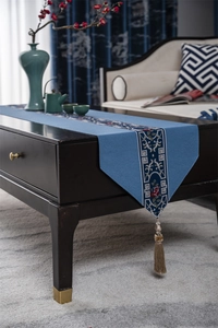 Detail of blue table runner with floral embroidery and hanging tassel on a wooden table