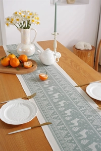 Detail of woven table runner with elk and forest pattern on a rustic wooden dining table