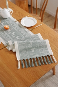 Detail of sage green table runner featuring reindeer patterns and handmade long tassels