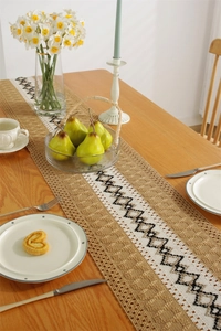 Detail of woven table runner with black diamond patterns and fringe on wooden table