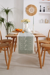 Detail of green and beige woven table runner featuring reindeer patterns and fringe tassels